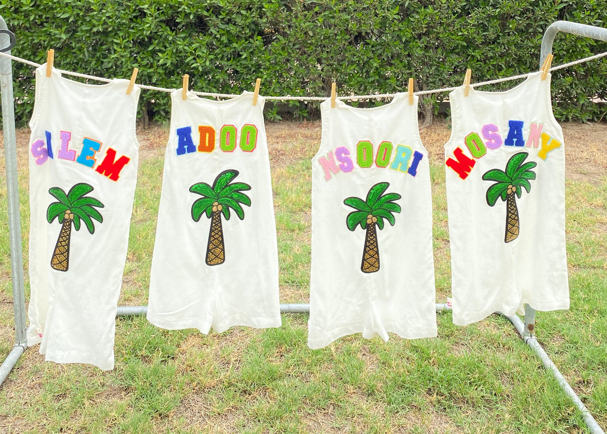 Four children in white palm-linen outfits with sequin palm tree patches, holding hands